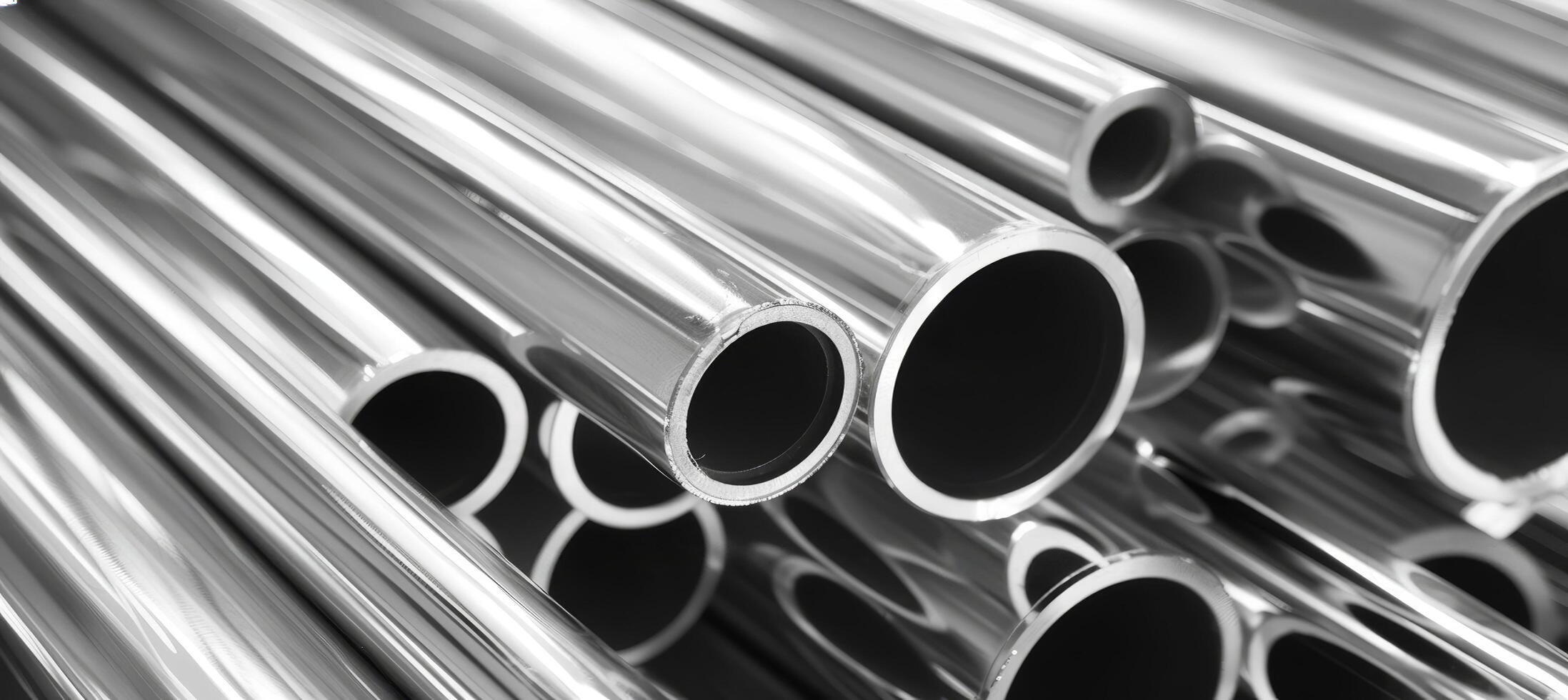 Professional warehouse shot of large stacks of polished stainless steel pipes of varying diameters with high-contrast metallic sheen.